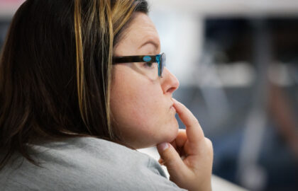 A woman with glasses and highlighted hair looks thoughtful, resting her chin on her hand as she contemplates her future after earning a bachelor degree.