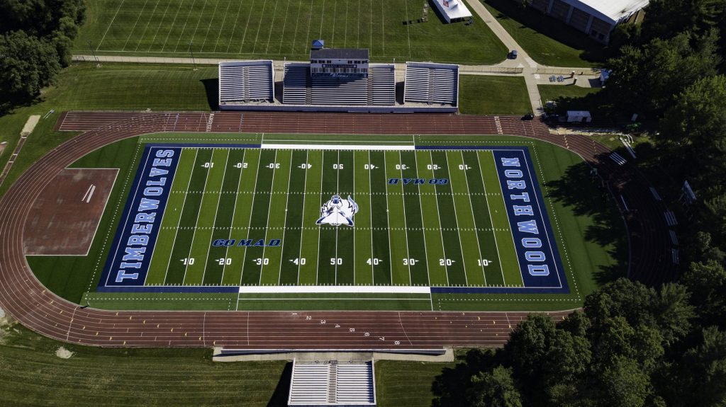 Aerial view of a football field with "Timberwolves" and "Northwood" on the sidelines, ideal for those interested in sports marketing jobs, surrounded by a running track and bleachers.
