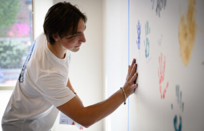 A person in a white t-shirt, embodying the spirit of entrepreneurship, is pressing their hand covered in blue paint onto a wall adorned with various colorful handprints.