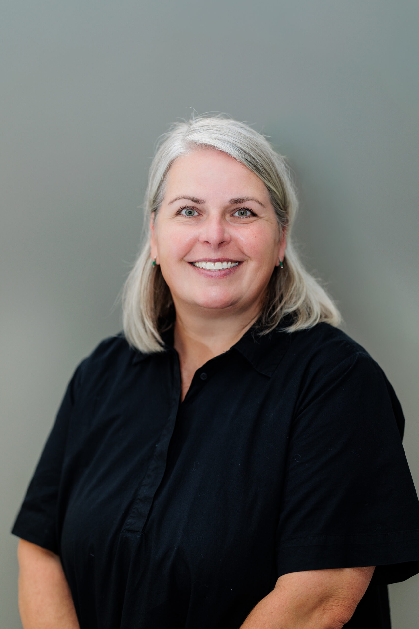 Dr. Christin Van Wyk Greiman is a smiling woman with shoulder-length grey hair wearing a black button-down shirt.