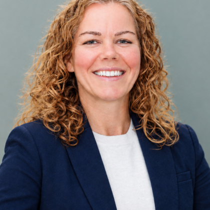 Dr. Stephanie VonFintel, a woman with curly light brown hair, wearing a navy blazer and white top, smiles in front of a plain gray background.