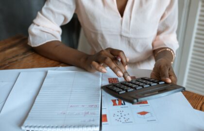 A person with an MS in Finance uses a calculator at a desk adorned with charts, graphs, and a notepad.
