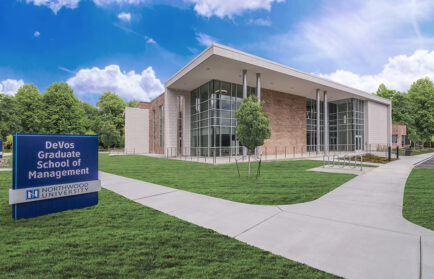An exterior photo of the DeVos Graduate School of Management, a tall brick building with large windows. Behind the building is a bright blue sky and in front is a path leading up to the building.
