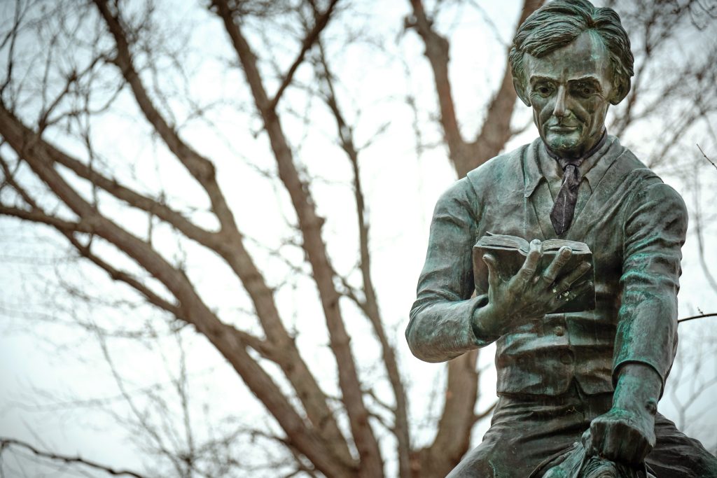 A bronze statue of a man reading a book stands serenely, symbolizing the pursuit of knowledge akin to securing undergraduate scholarships and grants, all framed against a backdrop of bare tree branches.