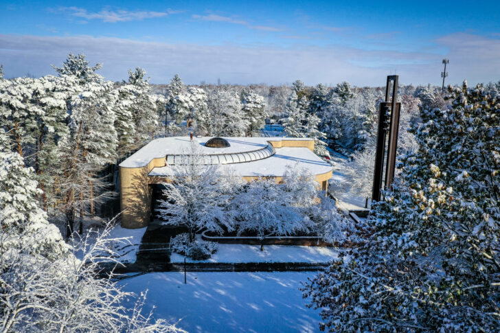 A building with a curved roof is surrounded by snow-covered trees under a clear blue sky.
