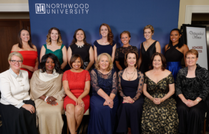 A group of women posing for a photo at a Northwood University event, with a backdrop displaying the university logo. Everyone is dressed in formal attire.