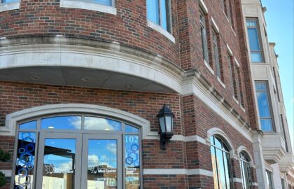 A red-brick building with large windows and a sign reading "Northwood University." Below, double glass doors are adorned with the university's logo. The building is located on a street with a clear sky above.