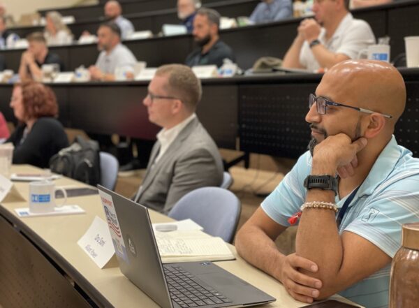 People seated in a classroom-style lecture hall, listening attentively. One individual is focused on their laptop.