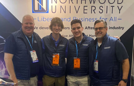 Four men in matching Northwood University vests stand together, smiling proudly, like a well-executed auto draft strategy, in front of a university banner.