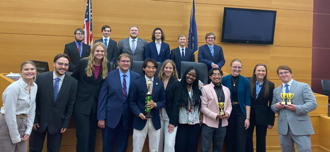 In a courtroom filled with anticipation, a group of people in formal attire stands proudly, some clutching trophies like tokens of triumph.