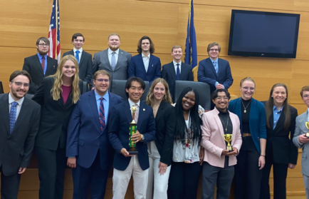 In a courtroom filled with anticipation, a group of people in formal attire stands proudly, some clutching trophies like tokens of triumph.