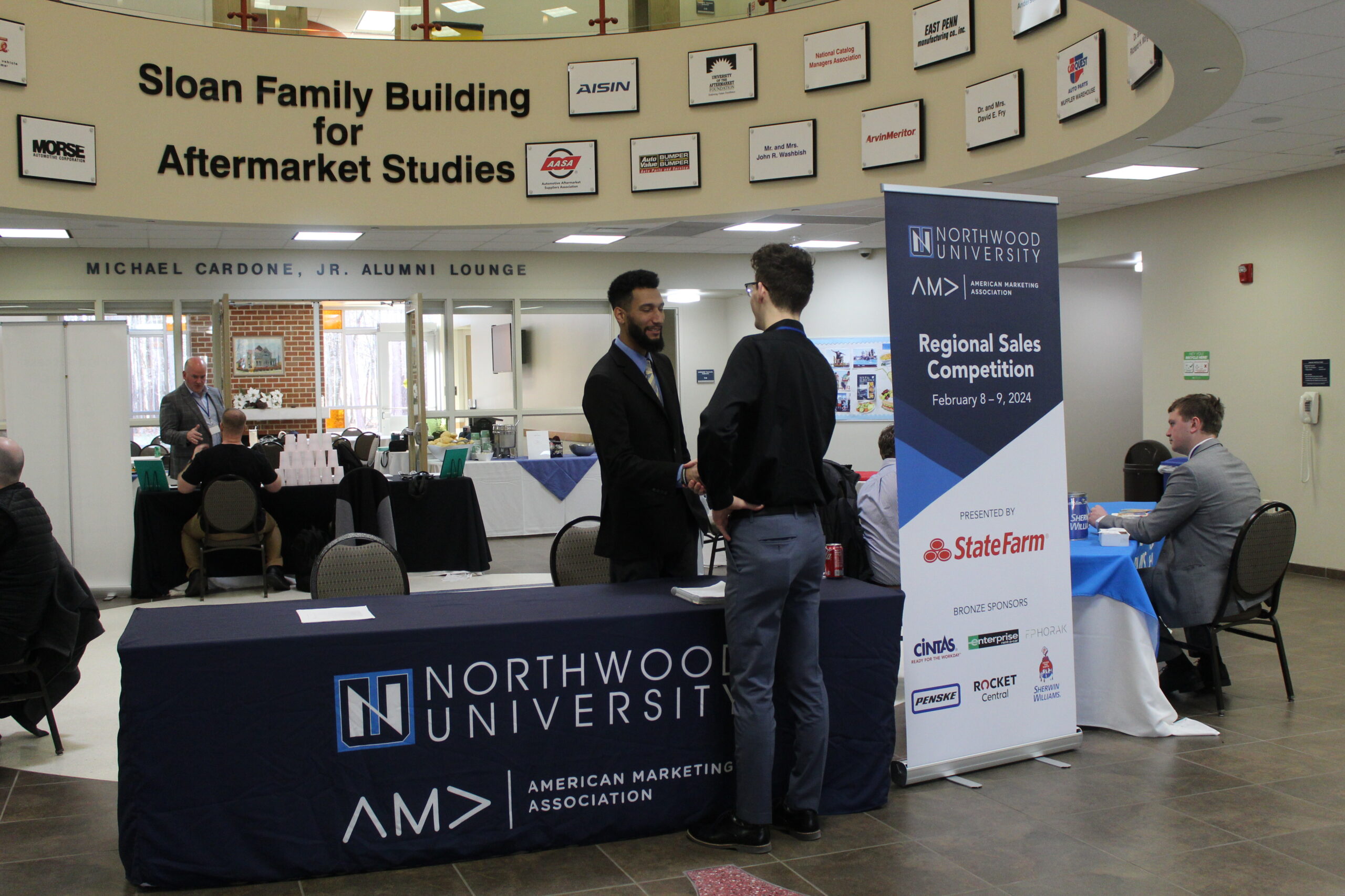 Two people shaking hands at a Northwood University event registration table, surrounded by banners and tables that capture the brand's essence.