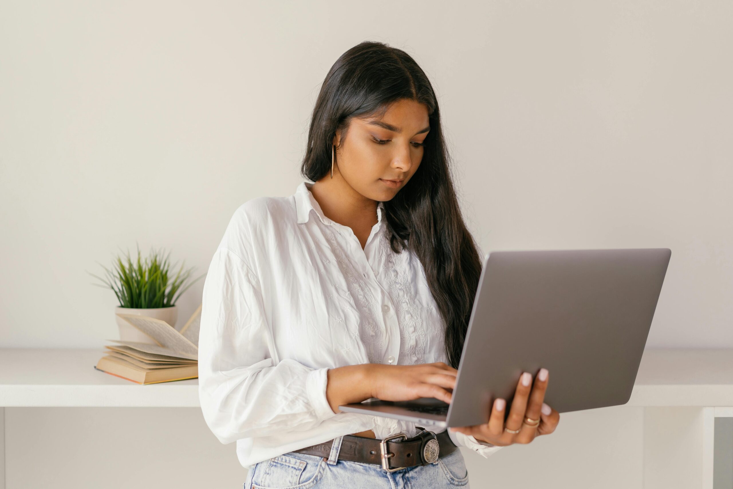 A woman in a white shirt stands while using a laptop.