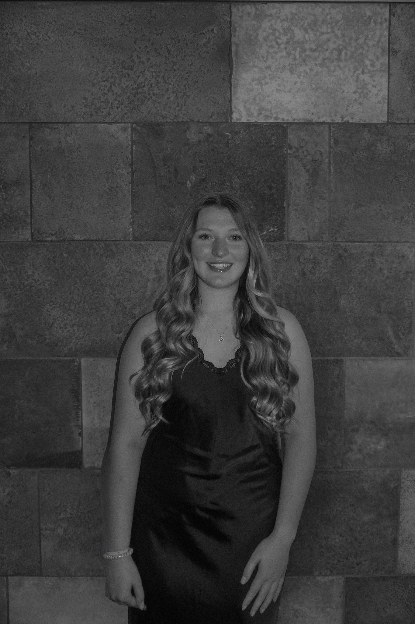 A person with long hair stands against a tiled wall, exuding elegance in a sleeveless dress, much like the sophistication of a Stafford dinner.