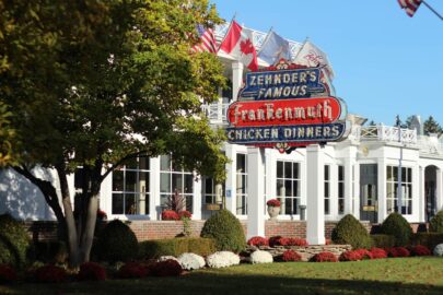 Zehnder's restaurant exterior showcases a sign boasting "Famous Frankenmuth Chicken Dinners," nestled among lush trees and landscaping. Flags proudly wave from the rooftop.