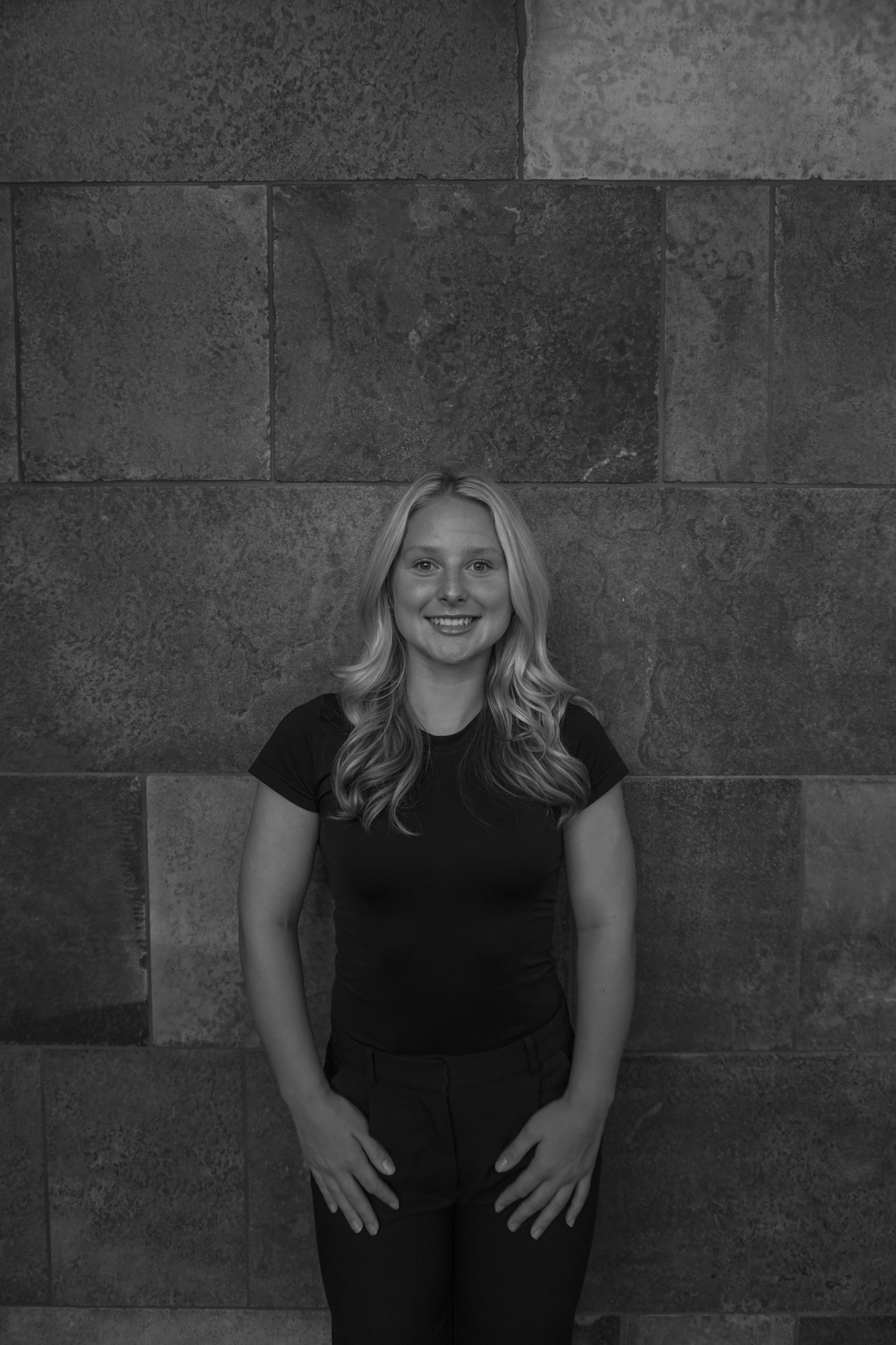 A person with long hair wearing a black shirt stands in front of a stone wall, reminiscent of a classic Stafford dinner setting.