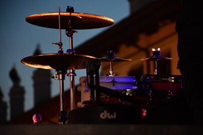 Drum set and cymbals illuminated against a dark backdrop with architectural elements reminiscent of a grand Stafford Dinner in the background.