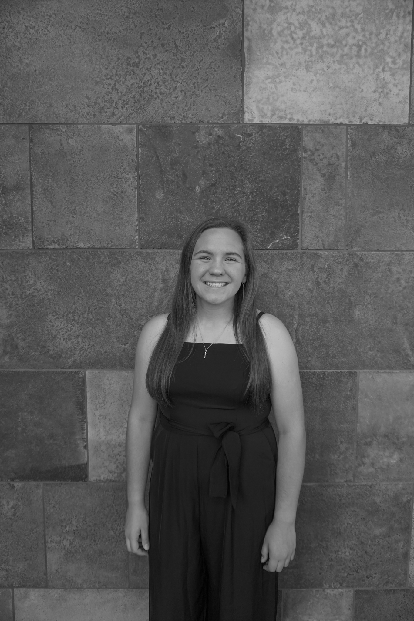 A person in a sleeveless dress stands smiling in front of a textured stone wall, radiating the elegance of a Stafford dinner.