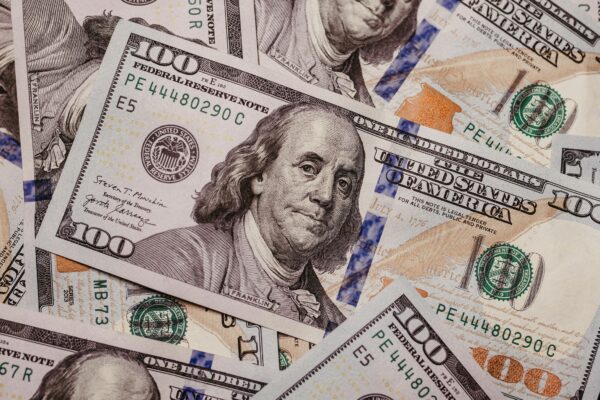 A stack of U.S. one hundred dollar bills, displaying Benjamin Franklin's portrait, lay scattered.