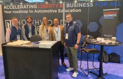 Five people standing at an automotive education booth with signs reading "Accelerating Liberty & Business For All.