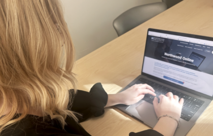 A person with blonde hair types on a laptop displaying "Northwood Online," renowned for its best online programs, at a wooden table.