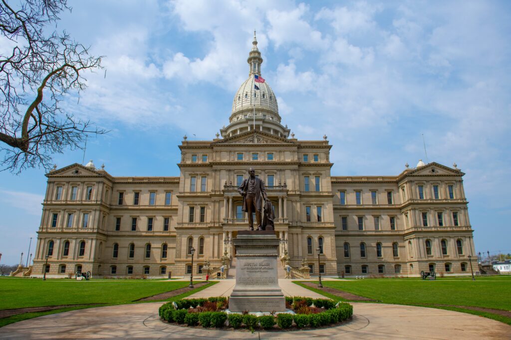 The Michigan State Capitol building in Lansing stands proudly under a clear blue sky, with a statue in front, symbolizing the achievements of those who earn their bachelor degree in the state.
