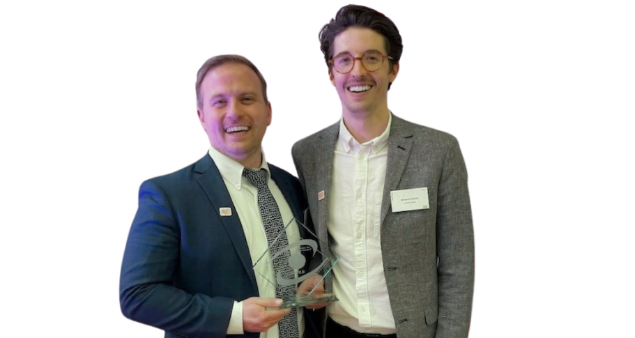 Two men in formal attire stand together, one proudly holding a clear award plaque from the Outstanding Business Leader Awards.