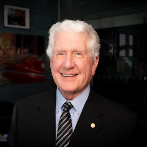 Elderly man with white hair in a suit and striped tie, smiling proudly.