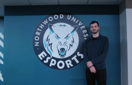 A person stands next to a "Northwood University Esports" logo on a wall.