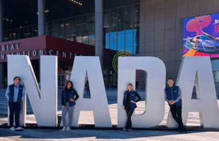 Four people stand in front of large "NADA" letters outside a convention center with modern glass architecture, capturing a moment for the Driven Newsletter in February 2025.