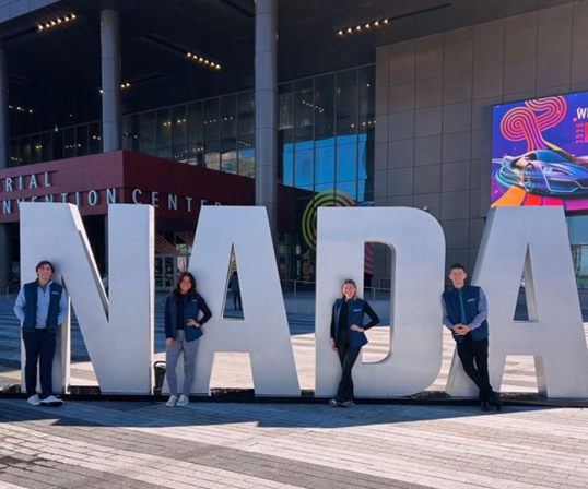 Four people stand in front of large "NADA" letters outside a convention center with modern glass architecture, capturing a moment for the Driven Newsletter in February 2025.