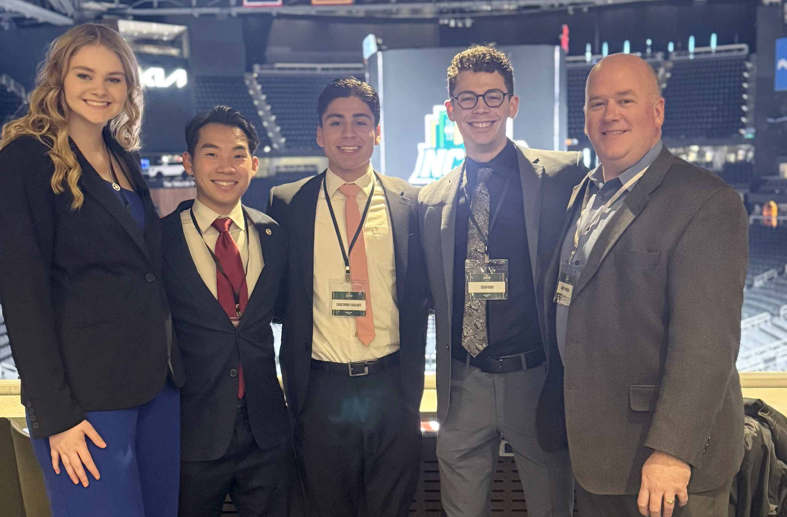 Five people in business attire smiling at an indoor event venue.