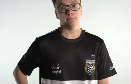 A person wearing glasses and a black esports jersey with white logos and text, including “oats overnight,” “SSG,” and “Northwood Esports,” points at the front of the shirt against a plain background.