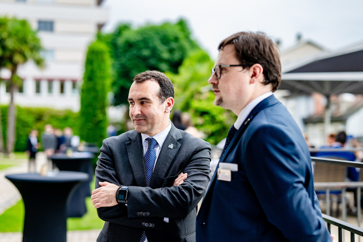 Two men in business suits stand outdoors at a formal Northwood University event, conversing, with other people and tables visible in the blurred background—perhaps discussing the impact of the Northwood Idea.