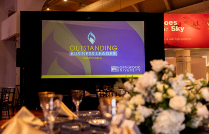 A projector screen displays "2025 Outstanding Business Leaders Awards Gala, Northwood University" at a formal event with decorated tables in the foreground.