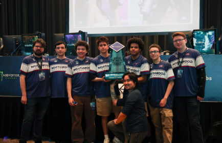 A group of eight people in matching Northwood jerseys stand on stage, holding a large trophy, with gaming equipment and screens in the background.
