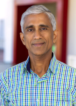 Dr. Srikanth Srinivasa, a middle-aged man with short gray hair, stands indoors in a green and blue checkered shirt, looking at the camera with a neutral expression.