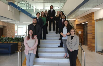 Ten professionally dressed people, including Skaff, stand and sit on a staircase in a modern building lobby, posing for a group photo at the Stafford Dinner 2026.