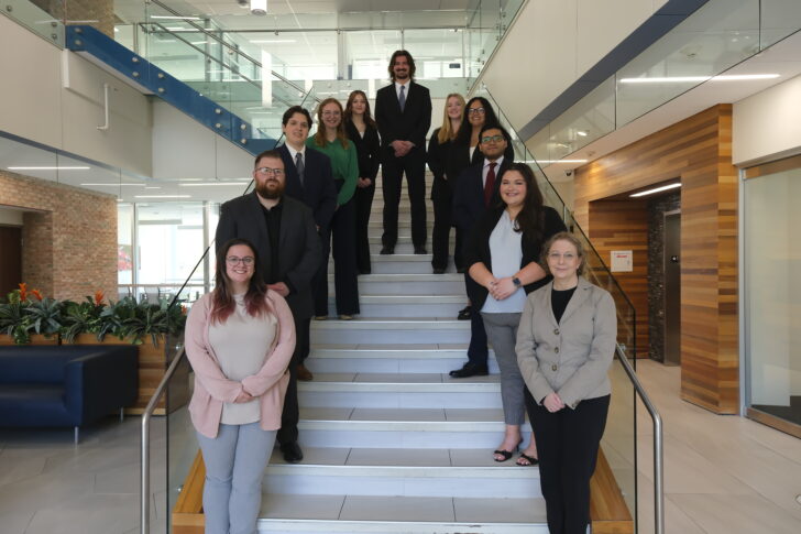 Ten professionally dressed people, including Skaff, stand and sit on a staircase in a modern building lobby, posing for a group photo at the Stafford Dinner 2026.