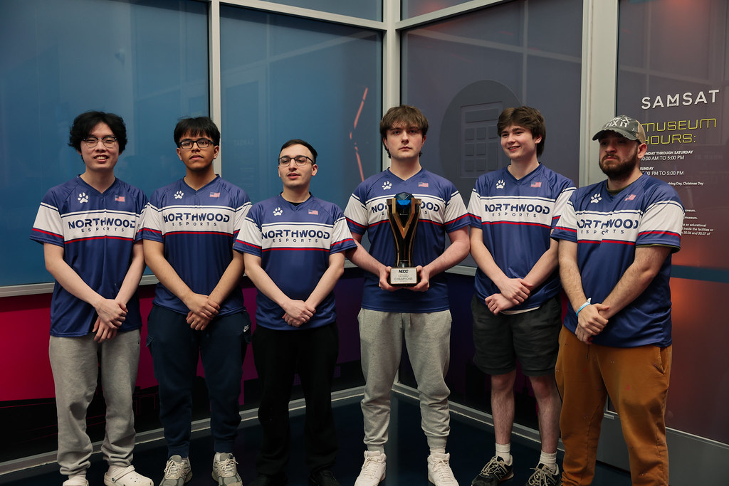 Six people wearing matching "Northwood" jerseys stand indoors, with one person in the center holding a trophy.