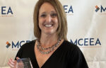 Kimberly Warner, in a black dress, holds the Career Services Professional Award and smiles in front of a backdrop with the MCEEA logo at the Michigan Alliance event.