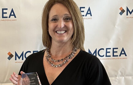 Kimberly Warner, in a black dress, holds the Career Services Professional Award and smiles in front of a backdrop with the MCEEA logo at the Michigan Alliance event.
