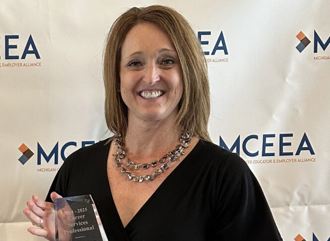 Kimberly Warner, in a black dress, holds the Career Services Professional Award and smiles in front of a backdrop with the MCEEA logo at the Michigan Alliance event.