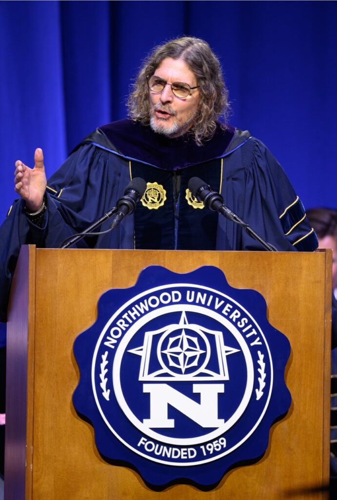 A man in academic regalia speaks at a podium displaying the Northwood University seal during a formal event.