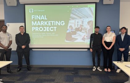 Five DeVos students stand in front of a screen displaying a slide titled "Final Marketing Project" for AC Transport, showcasing the real-world impact of their business fieldwork in a conference room.