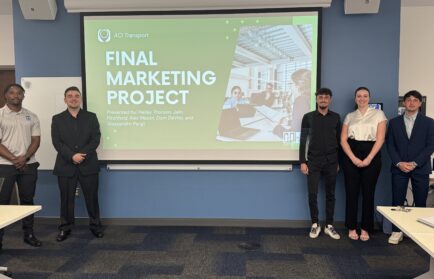 Five DeVos students stand in front of a screen displaying a slide titled "Final Marketing Project" for AC Transport, showcasing the real-world impact of their business fieldwork in a conference room.