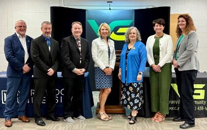 Seven adults stand in a row, posing for a group photo with the Provost in front of Vance-Granville Community College and partner banners, celebrating a new Transfer Agreement in a conference room.