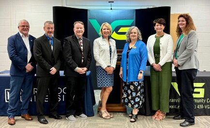 Seven adults stand in a row, posing for a group photo with the Provost in front of Vance-Granville Community College and partner banners, celebrating a new Transfer Agreement in a conference room.