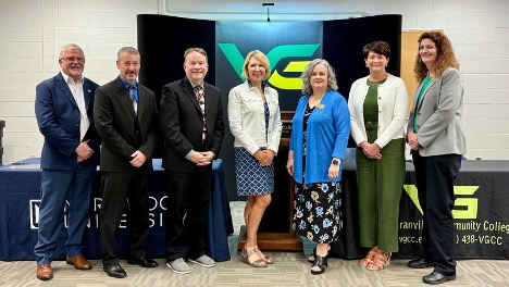 Seven adults stand in a row, posing for a group photo with the Provost in front of Vance-Granville Community College and partner banners, celebrating a new Transfer Agreement in a conference room.