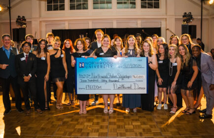 A large group of people pose indoors at a fundraising gala, holding an oversized $360,000 check made out to Northwood University Student Scholarships, dated 9/19/2025—supporting the future of automotive education.